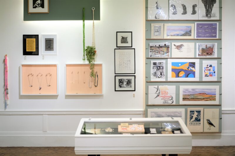 Bury Art Shop view of the wall with artworks and jewellery on display and for sale