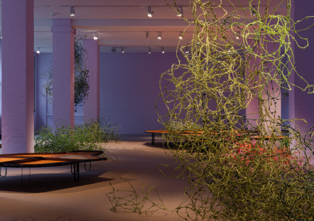 Installation view of 'Tending to the harvest of dreams' by Lungiswa Gqunta, displaying barbed wire wrapped in green fabric alongside metal tables in a purple room.