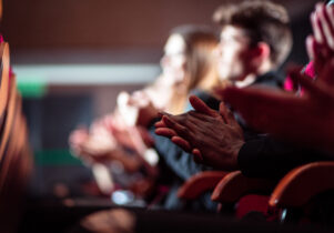 People in the theater. Side view. Dark tone. Focus on clapping hands.