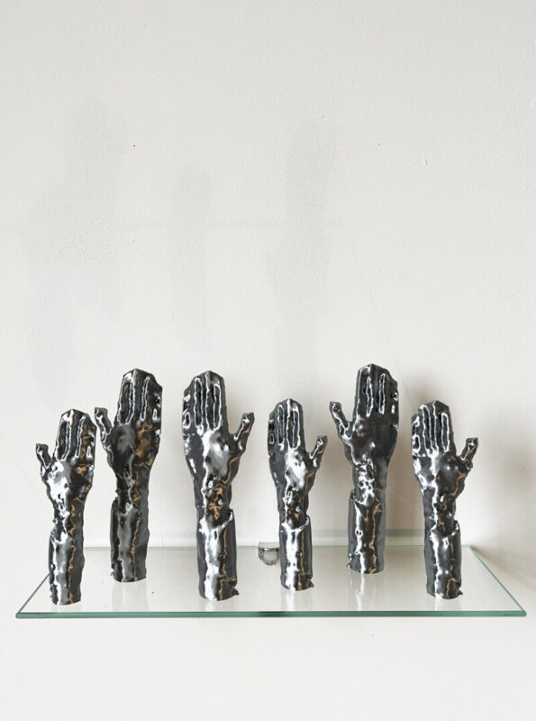 Six plastic sculptures of silver hands lined up on a shelf