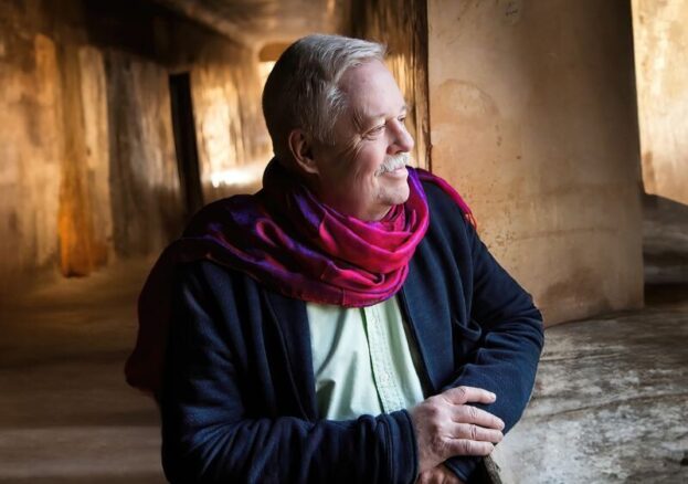 Image of Armistead Maupin looking to thier side, wearing a navy blue cardigan and magenta scarf