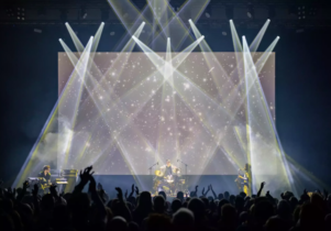 A band plays on a stage infront of a big crowd with lots of sparkling spotlights shining on them