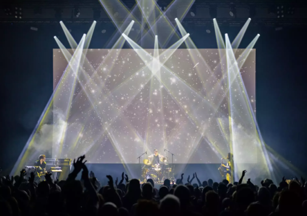 A band plays on a stage infront of a big crowd with lots of sparkling spotlights shining on them