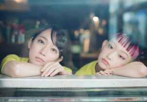 Two Japanese girls lean their heads on their hands looking out of a window, bored.