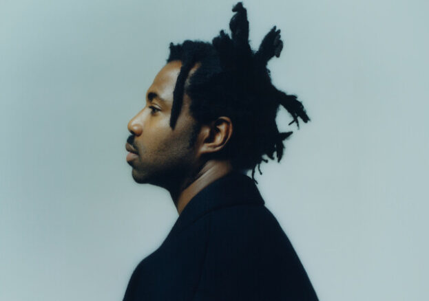 Side angle of artist Sampha on a light blue background