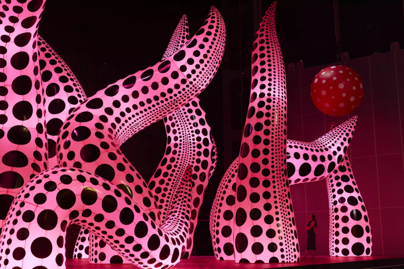 A woman looking at huge pink inflatable tentacles covered in polka dots