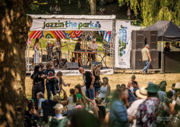 Image of a stage with a band playing and a crowd of audience members stood and sat down.