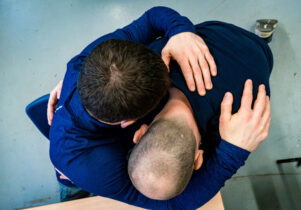 An image captured from overhead of two men embracing. One is seated, and the other is kneeling.