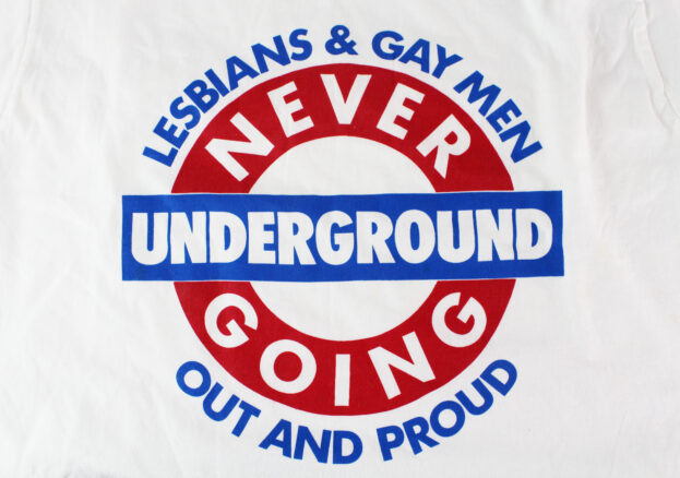 Red and blue logo on a t-shirt. The text reads Lesbians & Gay Men Out And Proud, Never Going Underground