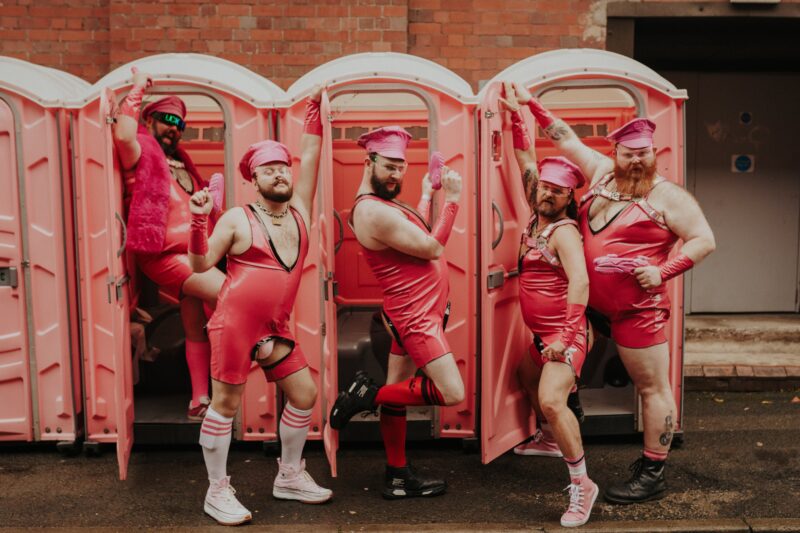 5 Fvck Pigs in pink posing in front of pink portaloos.