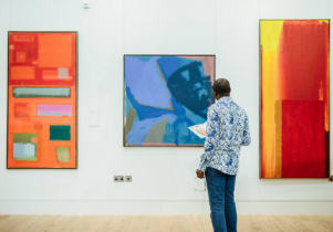 A visitor viewing three brightly coloured abstract artworks in The Stanley & Audrey Burton Gallery.