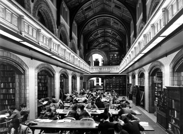 Black and white image of a traditional library setting with customers studying at desks.