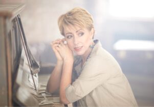 Photo of Nikki Iles with hands clasped at piano
