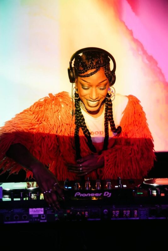A woman DJ looking down at decks with orange lighting