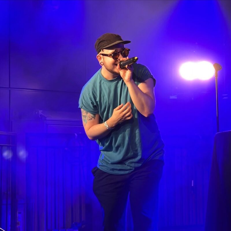 A performer singing into a mic with a blue background