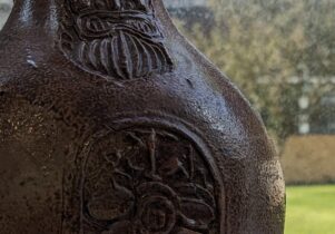 An earthern ware jar with a face and pattern on.