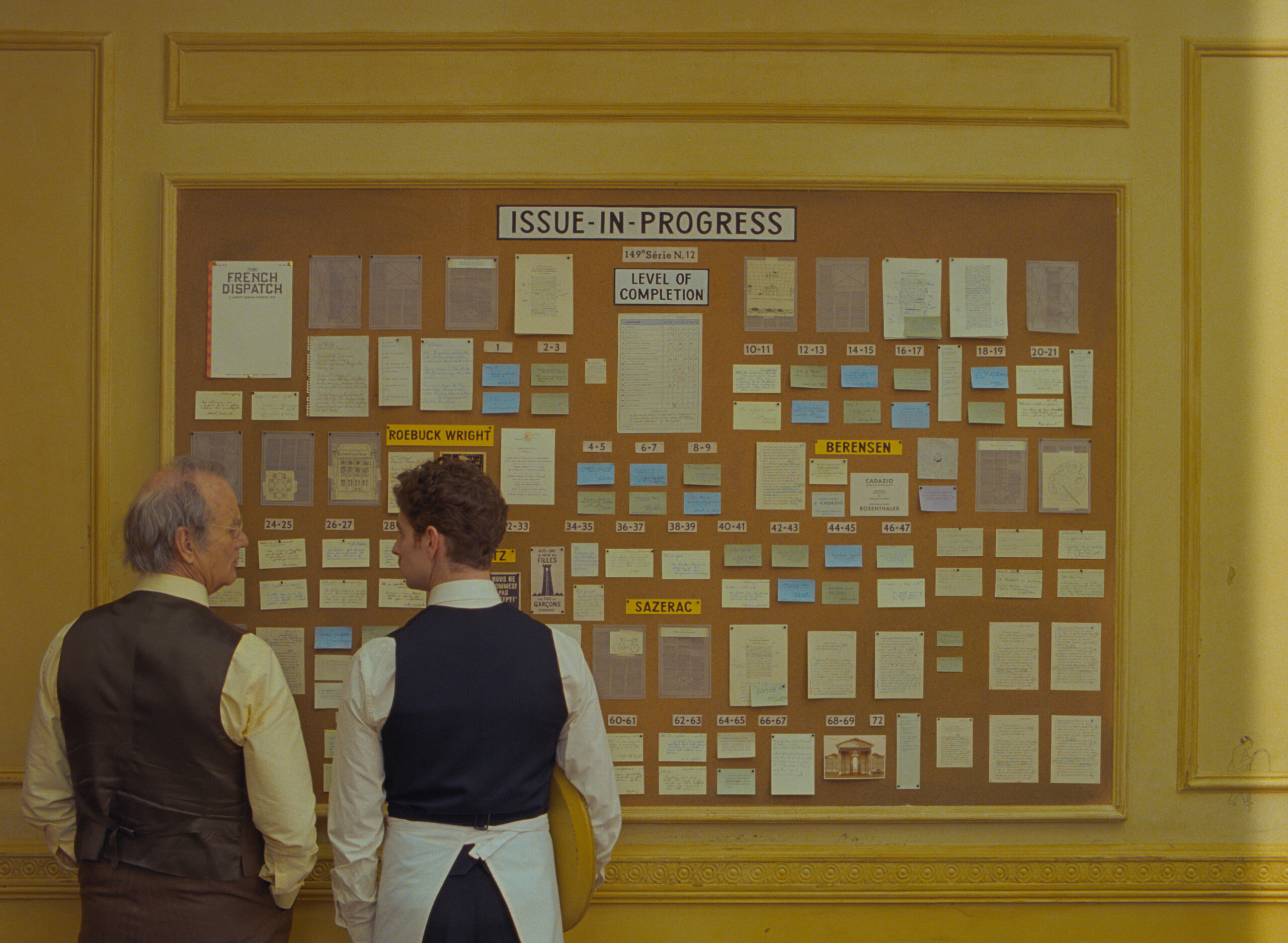 Two men pour stand next to each other against a board filled with paper notes.