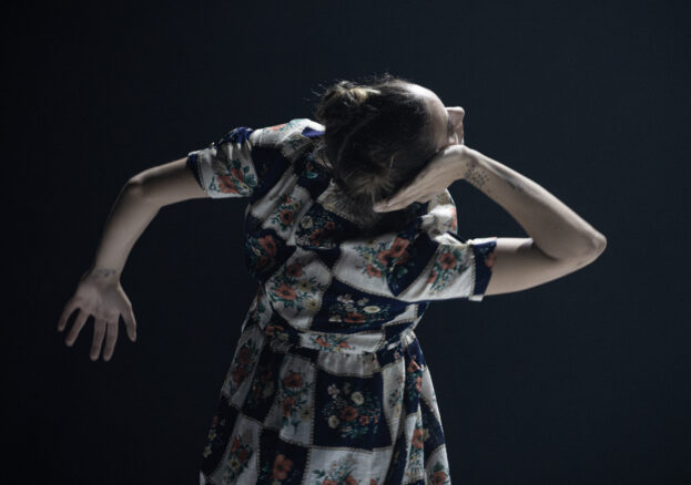 Equilibrio Dinamico | Through Her Eyes at the Riley Theatre: A woman dances with her hand to her ear in a graphic floral dress