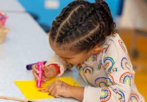 A photo of a girl coloring on a yellow piece of paper. Wellbeing Wonders at Z-arts