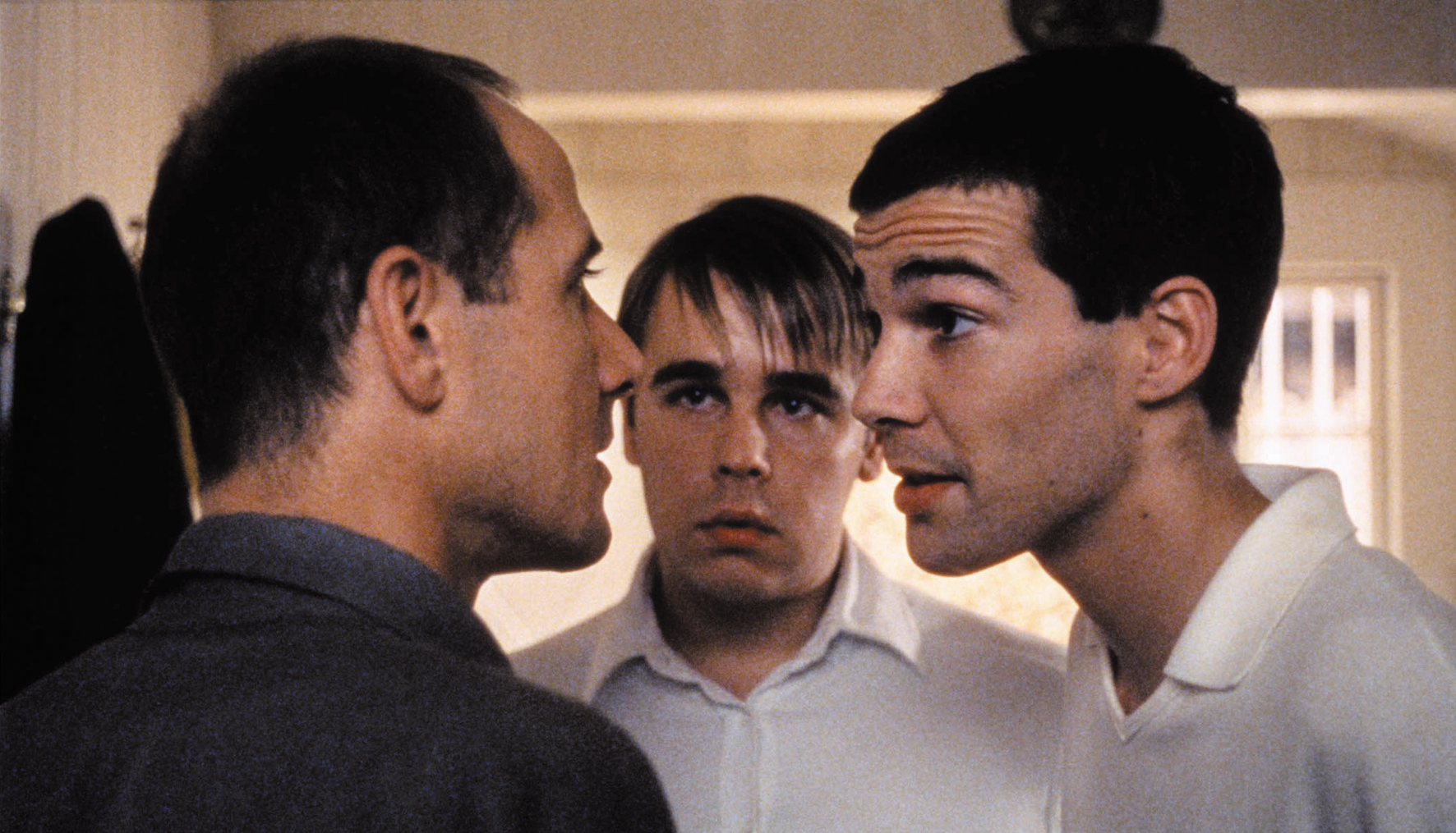 Three men stand closely together.