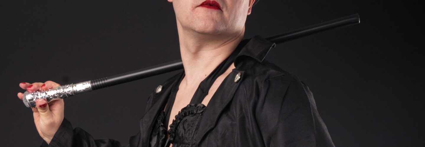 A man wearing red eye makeup dressed in black with a top hat and a cane over his shoulder.