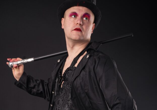 A man wearing red eye makeup dressed in black with a top hat and a cane over his shoulder.