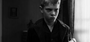 A young boy with a white sash around his left arm cries.
