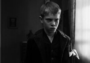 A young boy with a white sash around his left arm cries.