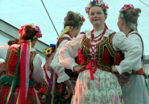 Four young female dancers in folk costumes, one looking at the camera