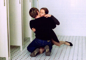 A man and a woman kiss sitting on a bathroom floor