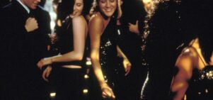 Two young women dance in a nightclub, smiling next to each other.