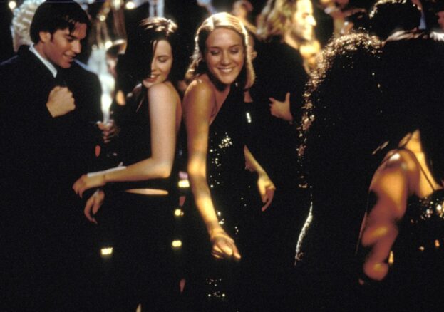 Two young women dance in a nightclub, smiling next to each other.
