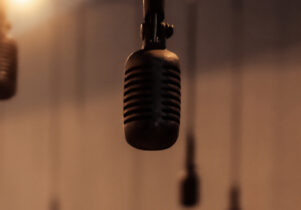 A series of microphones hang from the ceiling with a muted warm light in the background. 