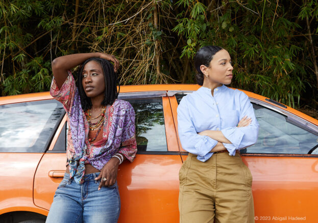 Two women stand next to an orange car.