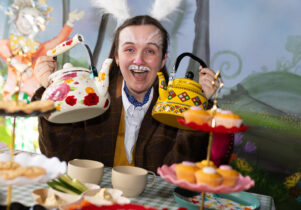 Mad Hatter's Tea Party at Z-arts A woman dressed as the white rabbit holds up two brightly coloured teapots to the camera.