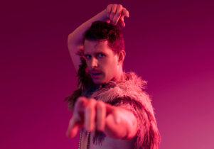 Buxton International Festival: Shorts at Pavilion Arts Centre. Pink lighting washes over a man, in flamboyant dress, looking and pointing at the camera; dancing.