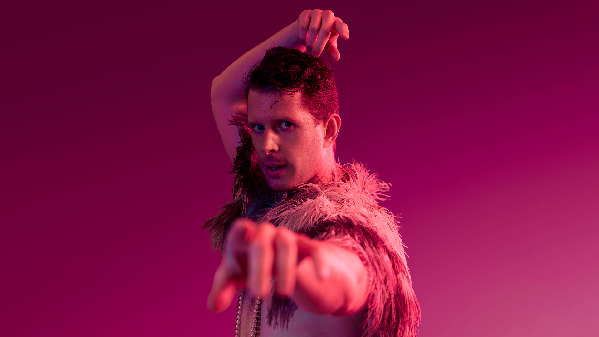 Buxton International Festival: Shorts at Pavilion Arts Centre. Pink lighting washes over a man, in flamboyant dress, looking and pointing at the camera; dancing.