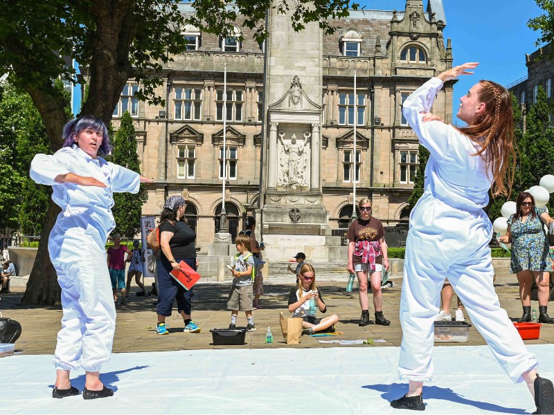 Two performers wearing white overalls, perform in front of a crowd.