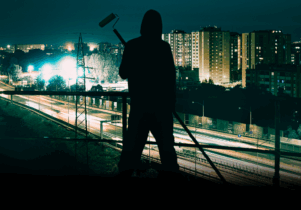 Graffiti artist GECO stood Infront of a city Scape at night 