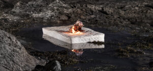 A white mattress is burning in a black rocky landscape.