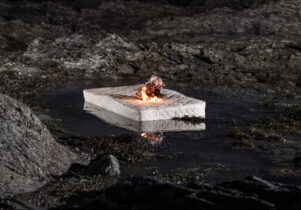 A white mattress is burning in a black rocky landscape.