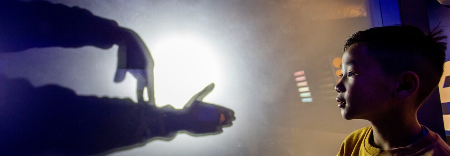 Boy looking at hands behind a shadow wall