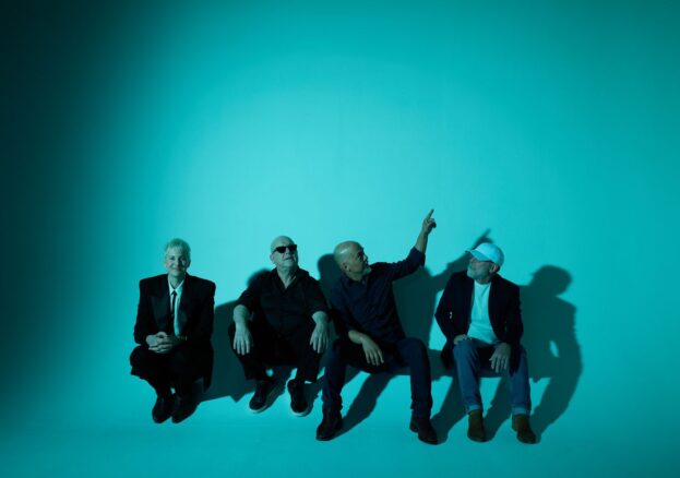 Four band members in a liminal space with a blue background.