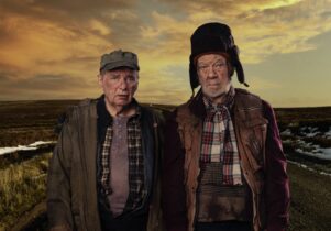 Two old men, in rough clothes, looking at the camera, against a cloudy sky