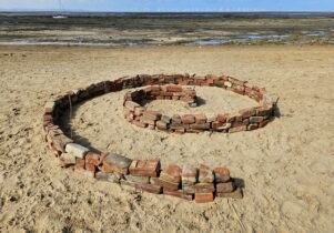 a beach. red bricks are laid out in a spiral shape on the sand.