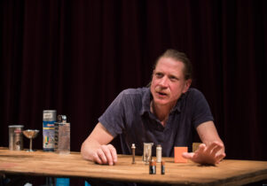 Selected Works: Table Top Shakespeare at Shakespeare North Playhouse : A man using objects like salt, pepper, batteries, thread, etc to enact famous Shakespeae plays. He is sat infront of a wooden table, with a serious expression
