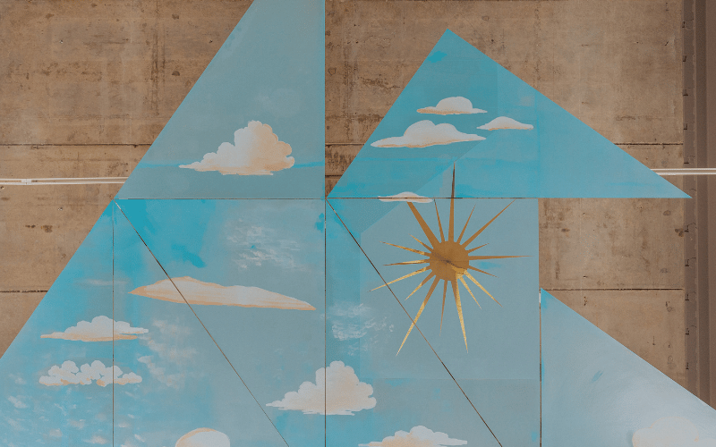 Blue triangles with white clouds on them against a beige backdrop. A gold sun is in the middle.