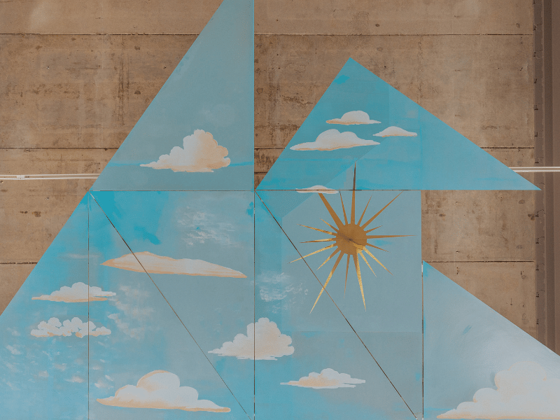 Blue triangles with white clouds on them against a beige backdrop. A gold sun is in the middle.