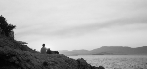 black and white image of person sitting on rock