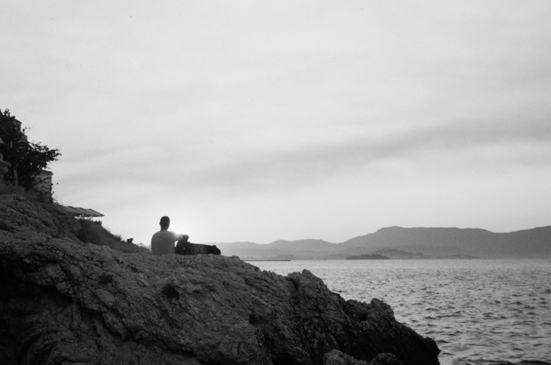 black and white image of person sitting on rock
